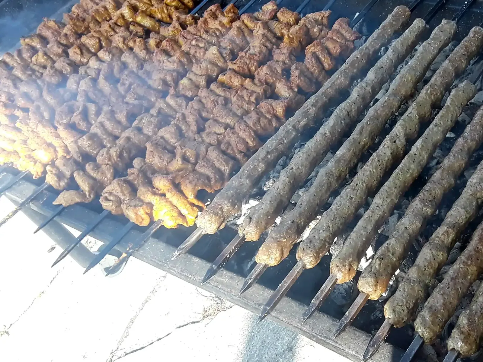 Rows of chicken tikka and seekh kabab skewers on a charcoal grill