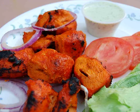 Chicken tikka pieces with charred edges, red onion, tomato, lettuce and raita