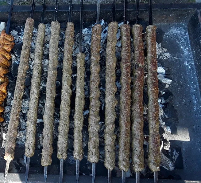 A row of seekh kabab skewers on a charcoal grill