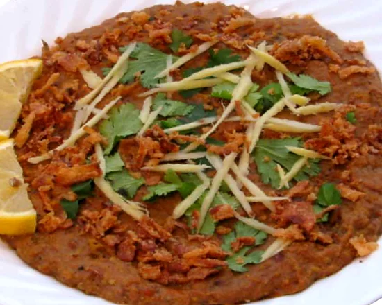 Haleem topped with fried onions, ginger strips, coriander and lemon wedges